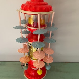 May include: A vintage red, white and blue plastic baby toy with spinning colourful balls and hanging plastic flowers. The toy has a clear plastic cylinder with a yellow ball inside.