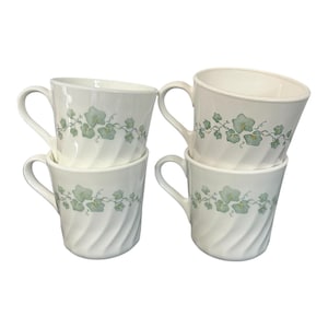 May include: Four white ceramic coffee mugs stacked. Each mug features a light green floral vine design and a spiral texture. The mugs have curved handles and are suitable for hot beverages.