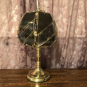 May include: A gold table lamp with a geometric, clear glass shade. The shade has a pattern of intersecting lines.