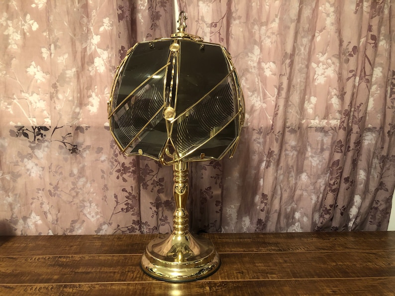 May include: A gold table lamp with a geometric, clear glass shade. The shade has a pattern of intersecting lines.