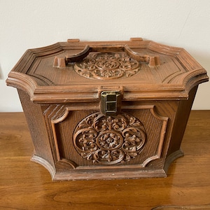 May include: A vintage wooden box with intricate carvings and a brass latch. The box has a handle on the top and is made of dark brown wood.