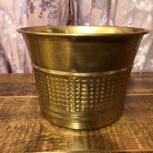 May include: A gold metal planter with a textured, embossed design. The planter is round and has a wide opening.