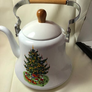 May include: White enamel teapot with a wooden handle and a Christmas tree design. The tree is decorated with ornaments, lights, and a train.