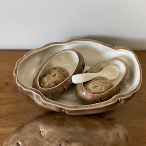May include: A brown ceramic serving dish shaped like a potato with two smaller potato-shaped bowls inside. The bowls have white interiors and are designed to hold condiments or sauces.
