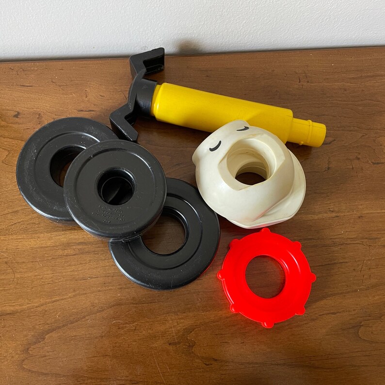 K&ouml;nnte beinhalten: Ein Satz schwarzer und roter Plastik-Stapelringe mit einer gelben und wei&szlig;en Plastikpumpe. Die Pumpe hat ein Gesicht mit geschlossenen Augen.