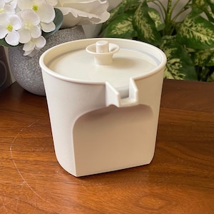 May include: A white ceramic creamer with a lid and a spout. The creamer has a smooth, rounded shape and a simple design.