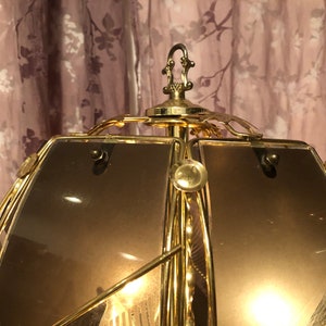 May include: A gold-toned metal lampshade with a geometric design. The lampshade has a frosted glass panel and a decorative finial on top.