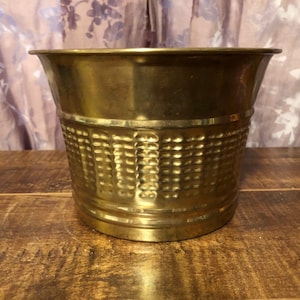 May include: A gold metal planter with a hammered texture. The planter has a round shape and a wide opening.
