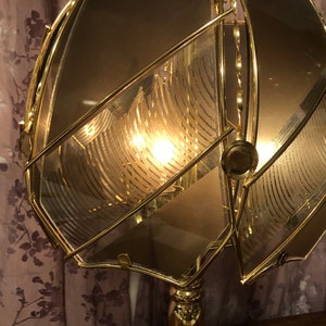 May include: A gold-toned metal lampshade with a geometric design. The lampshade is made of multiple pieces of glass that are joined together to create a unique and intricate pattern. The lampshade is illuminated from within, creating a warm and inviting glow.