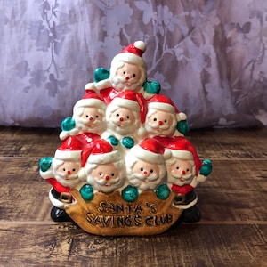 May include: A ceramic piggy bank shaped like a stack of Santas holding a bag with the text "Santa's Savings Club".