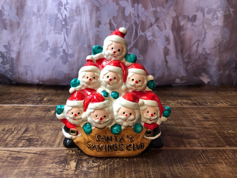 May include: A ceramic piggy bank shaped like a stack of Santas holding a bag with the text "Santa's Savings Club".