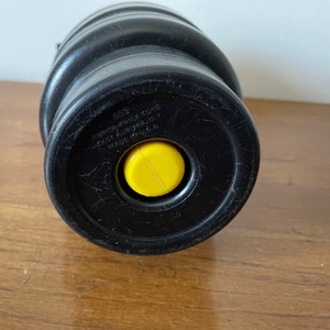 K&ouml;nnte beinhalten: Schwarzes Plastikspielzeug mit einem gelben Knopf. Das Spielzeug hat den Text "659 FISHER-PRICE TOYS EAST AURORA, NY MADE IN U.S.A." auf der Unterseite.