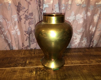 May include: A gold metal vase with a round body and a flared base. The vase is sitting on a wooden surface.