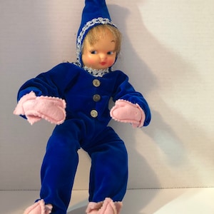 Peut inclure: Une poupée en velours bleu avec un chapeau rose et des mitaines roses. La poupée a un visage peint et des cheveux blonds.