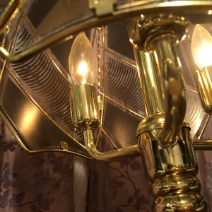 May include: A gold-toned table lamp with a geometric glass shade and three light bulbs. The lamp has a decorative base with a floral pattern.