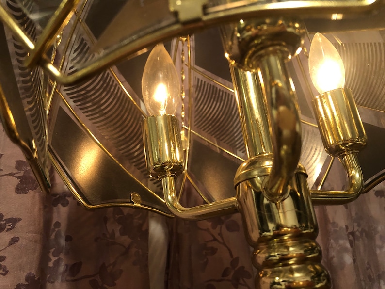 May include: A gold-toned table lamp with a geometric glass shade and three light bulbs. The lamp has a decorative base with a floral pattern.
