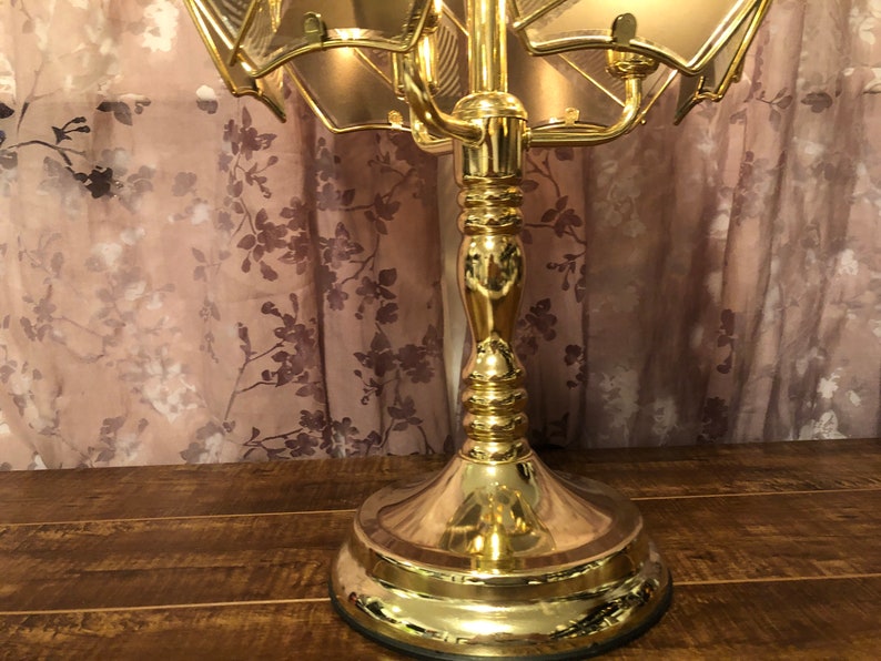 May include: A gold-toned table lamp with a multi-tiered, geometric, glass shade. The lamp has a decorative, ornate base.