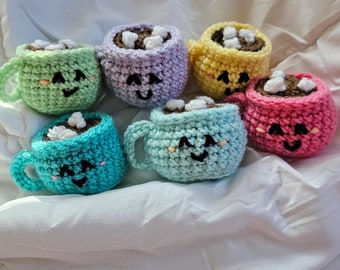 May include: Six crocheted mugs with smiling faces, each filled with brown liquid and white marshmallows. The mugs are in various pastel colors: green, purple, yellow, pink, blue, and light blue.