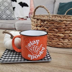 May include: Orange ceramic mug with a white design that says "Stay Spooky" with a skeleton hand making a shaka sign.