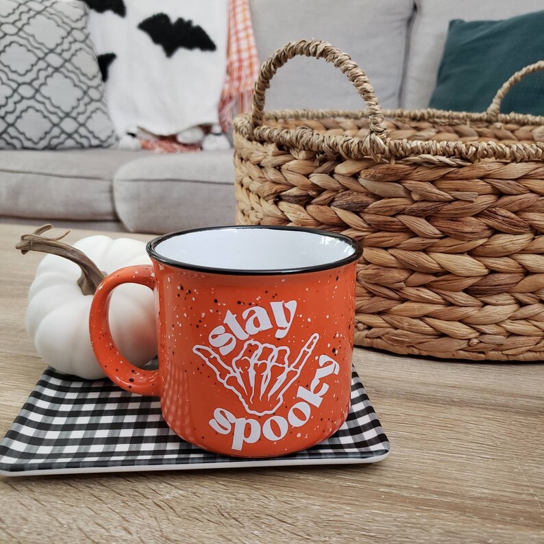 May include: Orange ceramic mug with a white design that says "Stay Spooky" with a skeleton hand making a shaka sign.