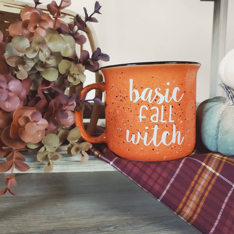 May include: Orange speckled ceramic mug with a black rim and handle. The mug has white text that reads "basic fall witch".