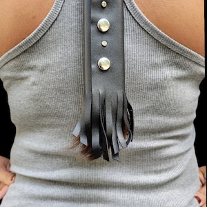 May include: Black leather accessory with silver-tone studs and fringe detail. The accessory is attached to a gray ribbed tank top. The fringe hangs down, adding a decorative element to the design.