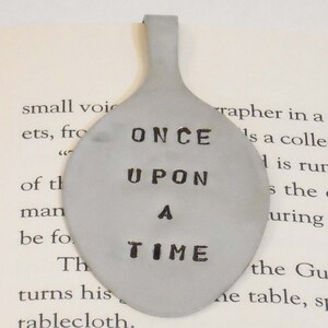 May include: A silver spoon bookmark with the words "Once Upon A Time" engraved on it.