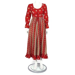 May include: A long red dress with a floral print and a gathered waist. The dress has long sleeves with ruffles at the cuffs and a ruffled hem.