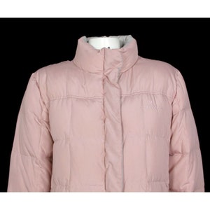 May include: A pink puffer jacket with a high collar and a zipper closure. The jacket has a quilted design and the brand name "Columbia" is embroidered on the left chest.