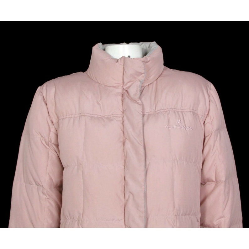 May include: A pink puffer jacket with a high collar and a zipper closure. The jacket has a quilted design and the brand name "Columbia" is embroidered on the left chest.