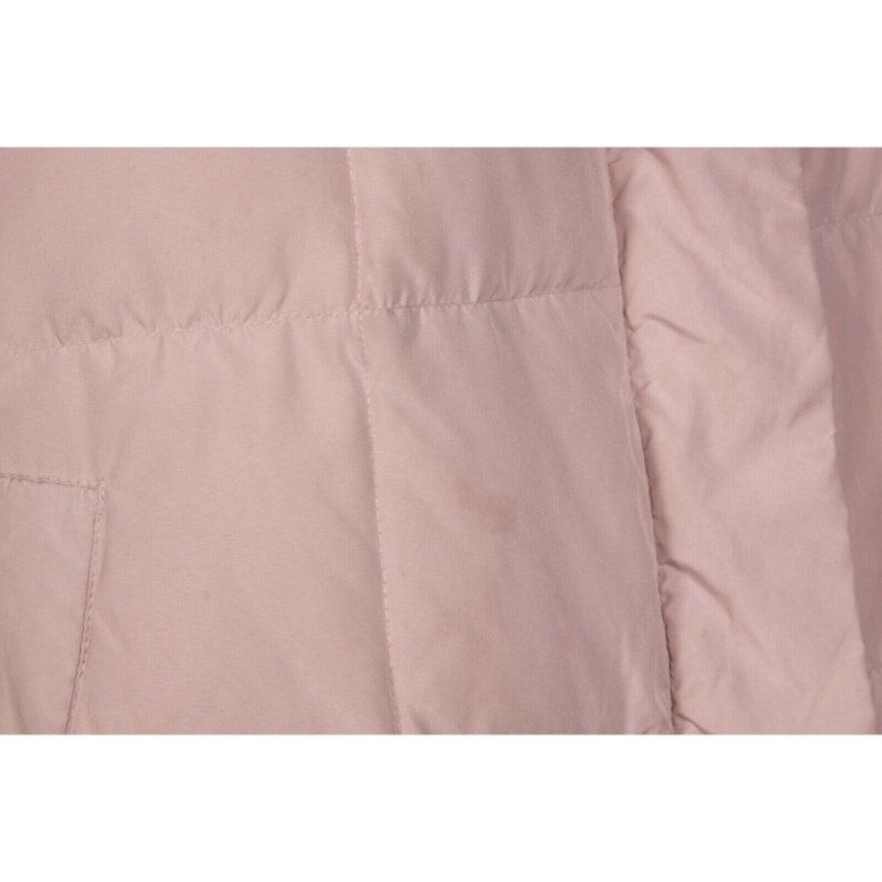 May include: A close-up of a pale pink quilted jacket. The jacket has a smooth, shiny finish and a subtle sheen.