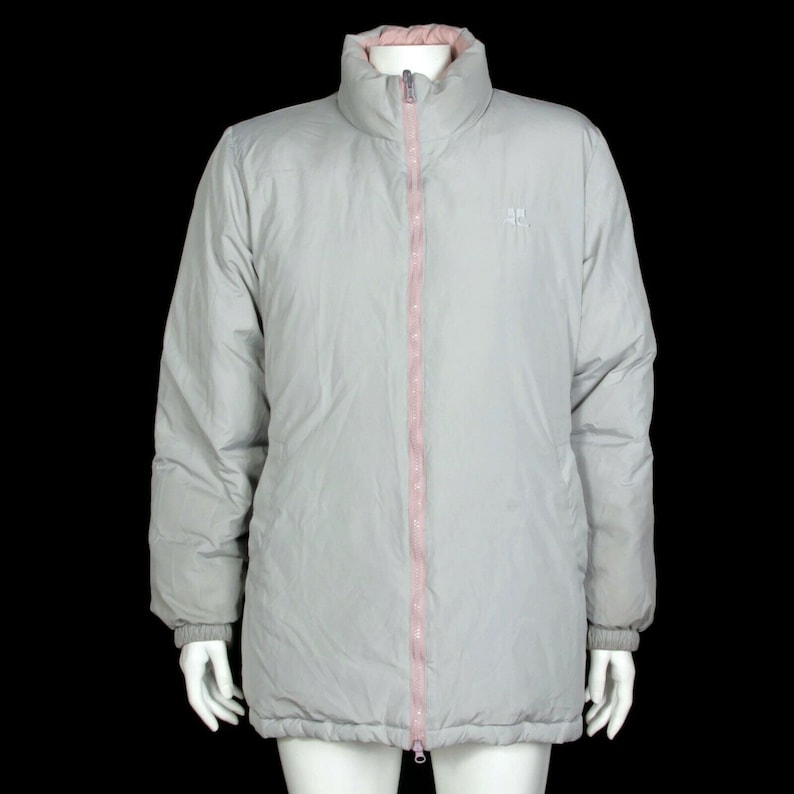 May include: A gray puffer jacket with a pink zipper and a small logo on the left chest. The jacket has a high collar and a long, slightly oversized fit.
