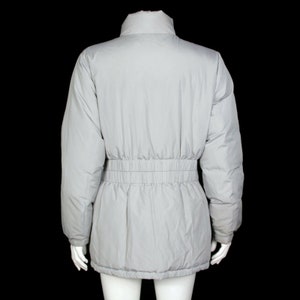 May include: A light gray puffer jacket with a cinched waist. The jacket has a high collar and long sleeves.