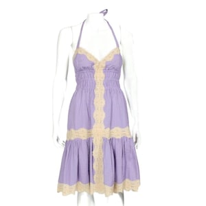 Könnte beinhalten: Ein lavendelfarbenes Neckholder-Kleid mit eng anliegendem Oberteil und ausgestelltem Rock. Das Kleid hat cremefarbene Spitzenbesätze am Ausschnitt, am Oberteil und am Saum. Das Kleid wird auf einer Schaufensterpuppe präsentiert.