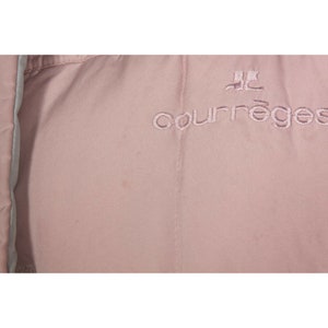 May include: A close-up of a pale pink jacket with the embroidered text "Courr&egrave;ges" in a darker pink.