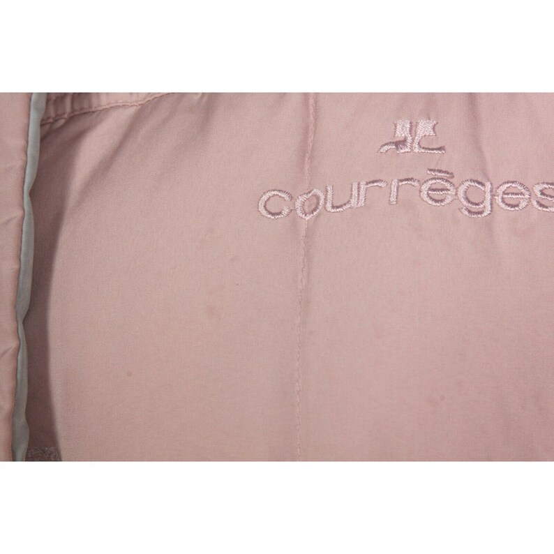 May include: A close-up of a pale pink jacket with the embroidered text "Courr&egrave;ges" in a darker pink.