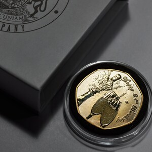 May include: A gold-colored coin with a design of two champagne glasses and the text "Happy 50th Anniversary" in a circular frame. The coin is in a clear plastic case.