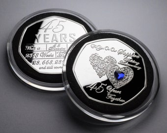 Puede incluir: Una moneda de plata con una piedra preciosa de zafiro azul en el centro de dos corazones entrelazados. La moneda está inscrita con "For You On Our Sapphire Wedding Anniversary" y "45 Years Together". El reverso de la moneda está inscrito con "45 Years" y "That is... 45 Decades 2348 Weeks 28,668,289 and still counting".