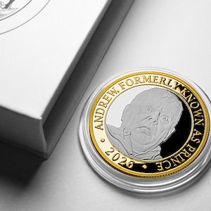 Puede incluir: Una moneda de plata y oro con un retrato de un hombre, el texto "ANDREW FORMERLY KNOWN AS PRINCE" y el año 2026. La moneda está en una funda transparente, junto a una caja blanca.