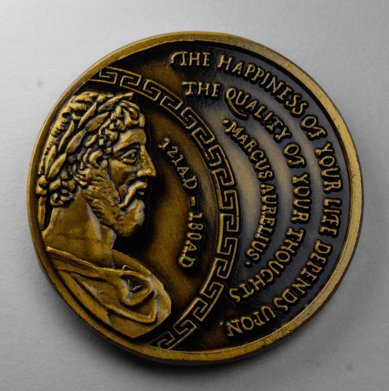 May include: A gold-colored coin with a profile of Marcus Aurelius, a Roman emperor, and the inscription "THE HAPPINESS OF YOUR LIFE DEPENDS UPON THE QUALITY OF YOUR THOUGHTS MARCUS AURELIUS 121AD-180AD".
