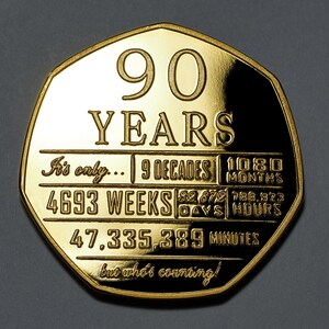 May include: A gold-coloured coin with the inscription "90 YEARS" and a breakdown of the time in years, decades, months, weeks, days, hours, and minutes. The inscription reads "It's only... 9 Decades 1080 Months 4693 Weeks 32,879 Days 788,923 Hours 47,335,389 Minutes but who's counting!"