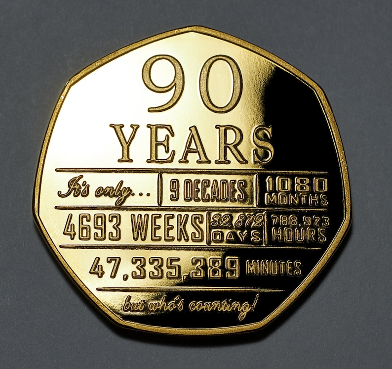 May include: A gold-coloured coin with the inscription "90 YEARS" and a breakdown of the time in years, decades, months, weeks, days, hours, and minutes. The inscription reads "It's only... 9 Decades 1080 Months 4693 Weeks 32,879 Days 788,923 Hours 47,335,389 Minutes but who's counting!"
