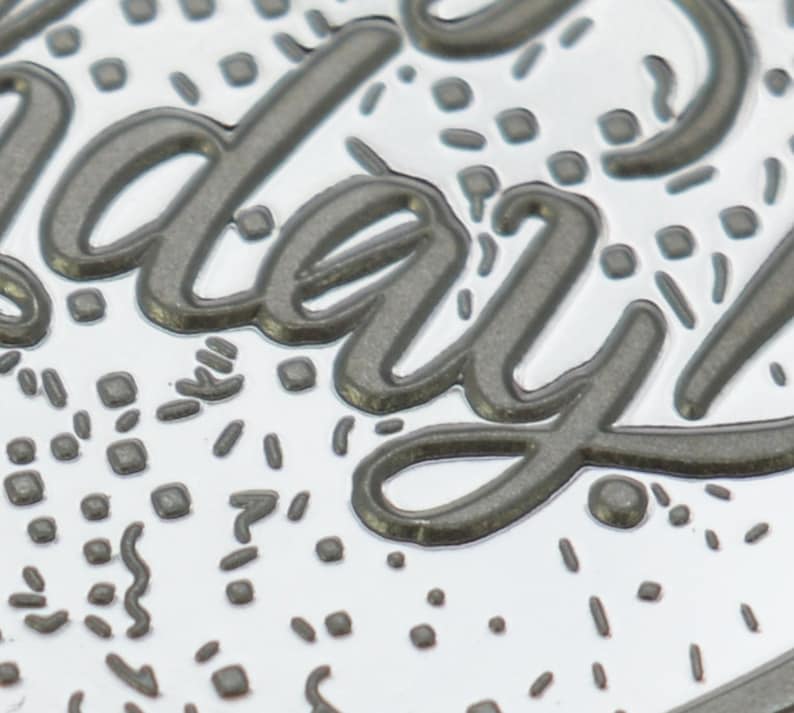 May include: A silver metal charm with the word "everyday" embossed in a dark gray color. The charm is decorated with a confetti-like pattern of small gray squares and lines.