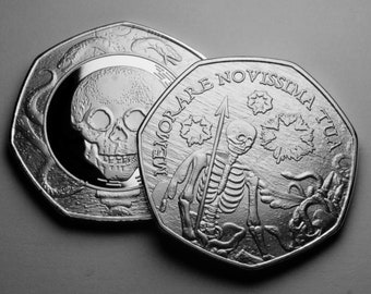 Op de afbeelding: Twee zilveren munten met een schedel- en skeletontwerp. De eerste munt toont een schedel met een slang eromheen gewikkeld. De tweede munt toont een skelet dat een speer vasthoudt met de tekst "MEMOARE NOVISSIMA TUA" rond de rand.