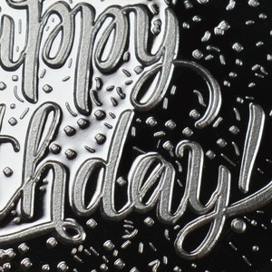 May include: Close-up of a silver embossed greeting card with the text "Happy Birthday!" on a black background.