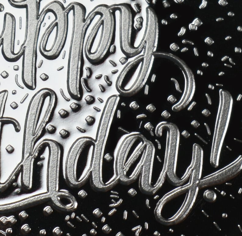 May include: Close-up of a silver embossed greeting card with the text "Happy Birthday!" on a black background.