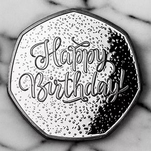 May include: A silver coin with a celebratory design. The coin features the words "Happy Birthday!" in a decorative script.