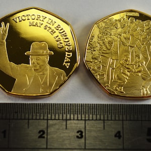May include: Gold-colored commemorative coin featuring Winston Churchill on one side and a crowd of people on the other. The coin reads "Victory in Europe Day May 8th 1945".