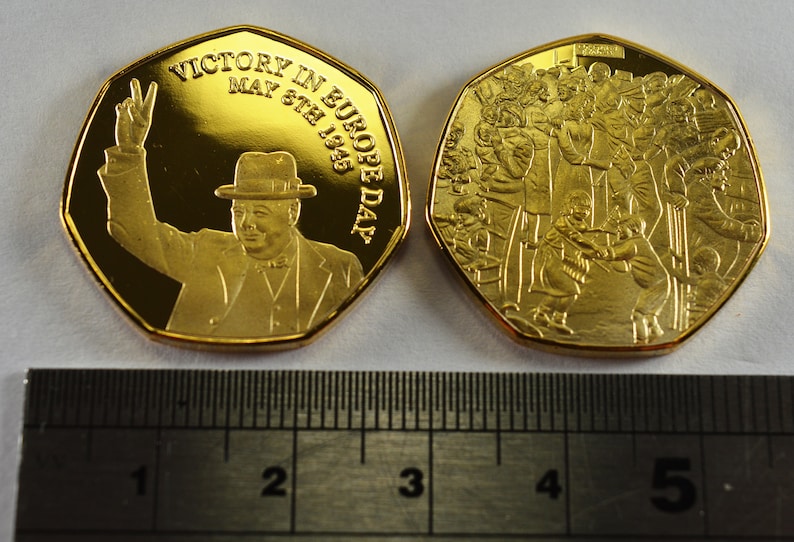 May include: Gold-colored commemorative coin featuring Winston Churchill on one side and a crowd of people on the other. The coin reads "Victory in Europe Day May 8th 1945".