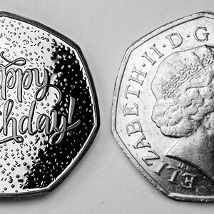 May include: A silver coin with a domed, octagonal shape. One side features the inscription "Happy Birthday!" in a stylized font. The other side features a profile of Queen Elizabeth II and the inscription "ELIZABETH II D.G. REG. F.D. 2002".
